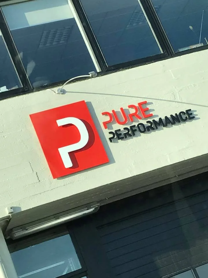 Skilti Pure Performance á húsvegg